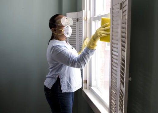 Adult wearing goggles, yellow gloves and a mask cleaning the window.