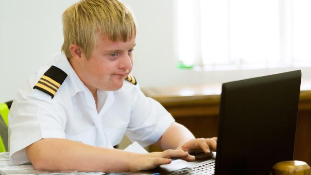 A teen wearing a shirt with epaulettes using a laptop