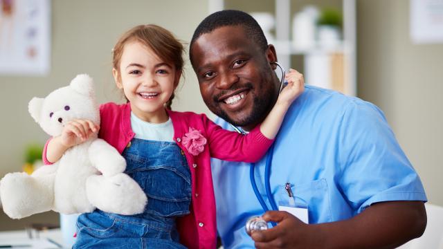 Child hugging a teddy bear with left arm near healthcare provider's neck