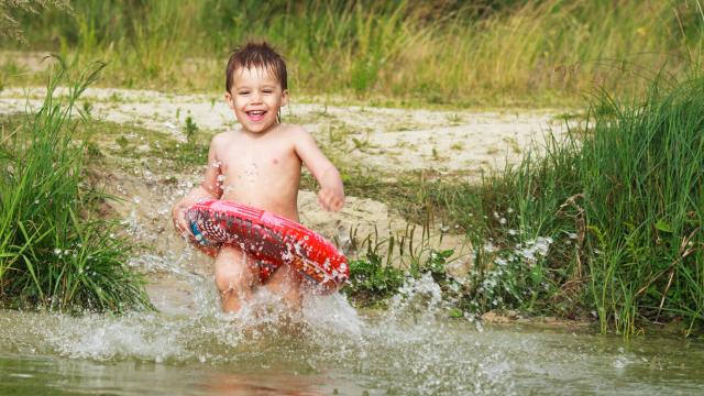 A happy young child wearing an inner tube running into a lake.