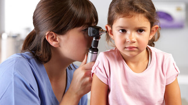 A doctor checking child's ear with otoscope.