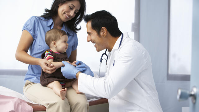 Adult holding baby while doctor does examination