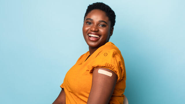 A smiling adult with sleeve rolled up showing band aid covered vaccine spot