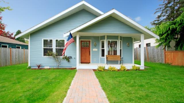 light blue house with white trim and porch with a flag on porch