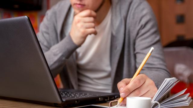 A person writing notes in the book while looking at the laptop.