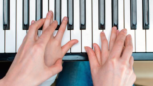 A pair of hands over child's hands on piano keys.