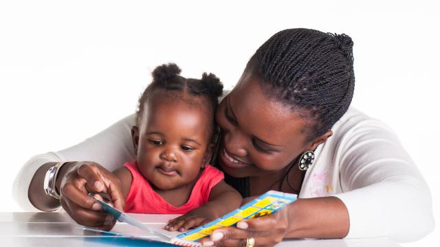 An adult with toddler on lap reads a book on white table
