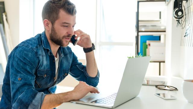 An adult works on laptop while talking on phone in the office