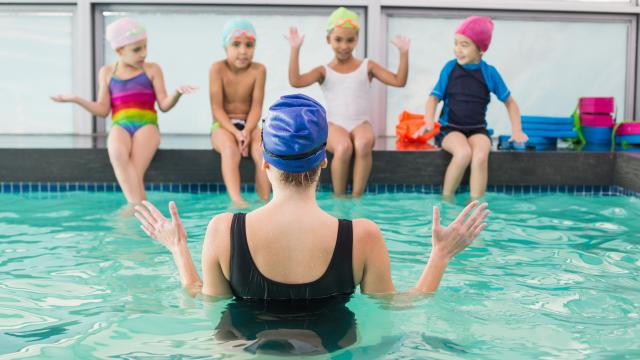 An instructor explaining to four young children sitting on the edge of a swimming pool.