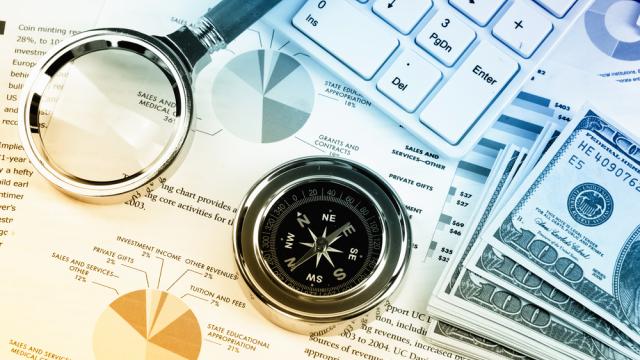 A compass set on paper with chart pie, pile of 100 dollars, magnifying glass and calculator.