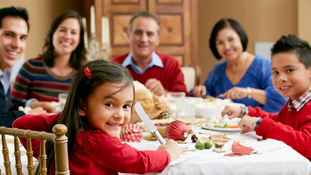 Four smiling adults and two smiling children enjoying a meal at home.