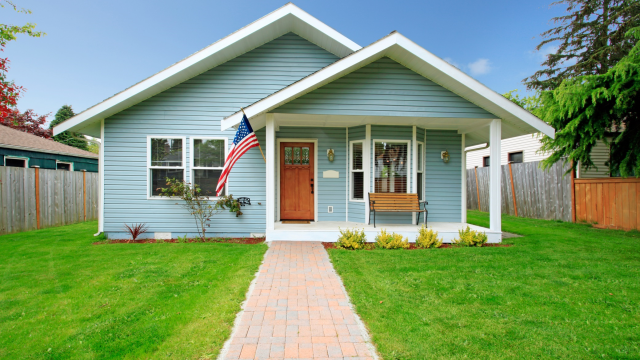 A blue home flying the American flag in the front porch with wooden fence