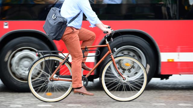 An adult with a briefcase riding bicycle next to a bus.