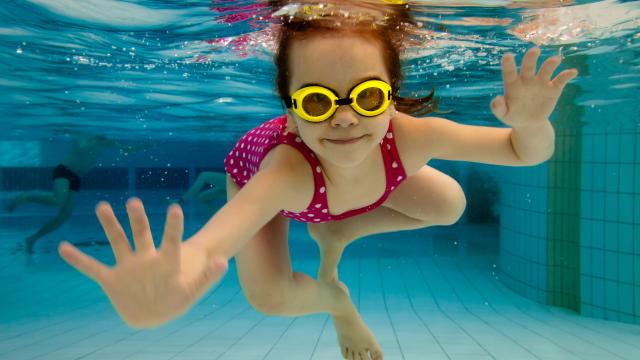 A happy child swims underwater in a pool.