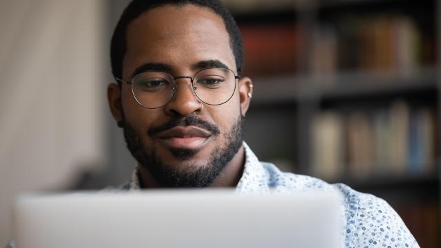 Close up of a young adult wearing glasses and working on a laptop