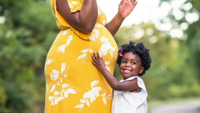 Smiling child hugging a pregnant belly