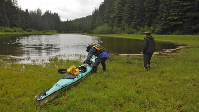 Two adults launching a kayak in the marsh