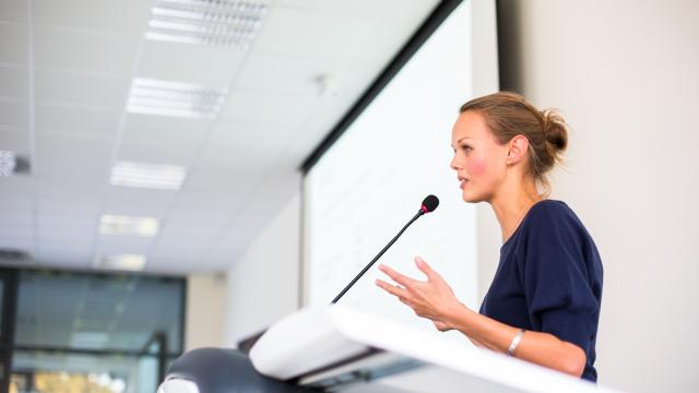 An adult speaks into a microphone in front of a room