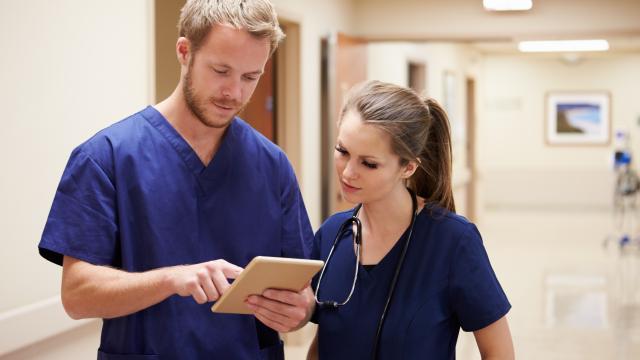 Two medical staffs discussing items on tablet in a corridor.