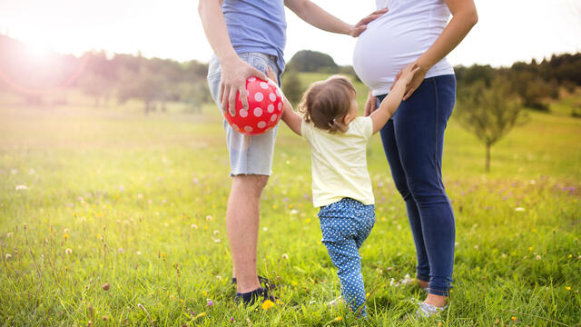 Family standing in circle holding hands with adult hand on pregnant belly