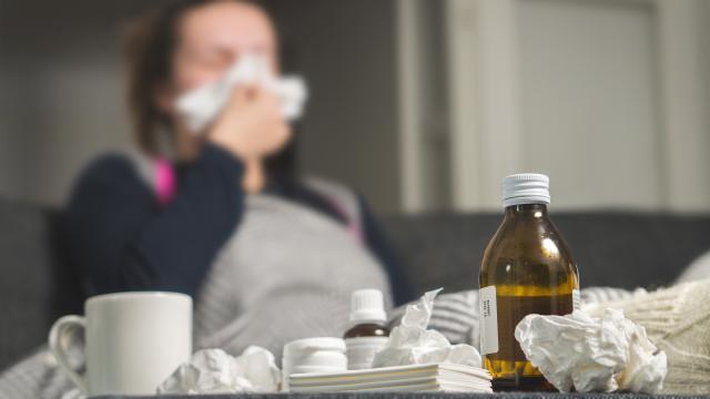 Ill adult blowing nose with used tissues and meds on table.