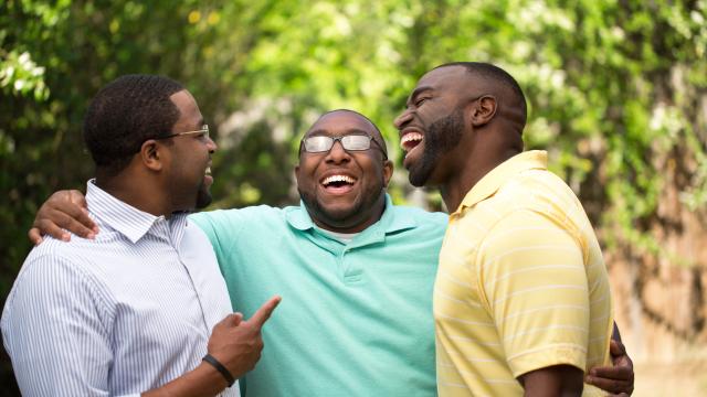 Three adults hugging and laughing outside.