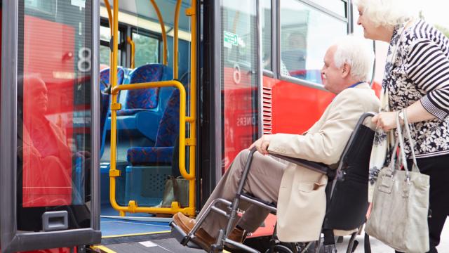 A senior pushed a wheelchair with a senior up on a bus ramp