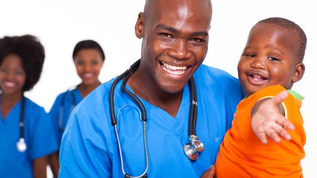 A smiling doctor holds a smiling child with two medical personnel in the background