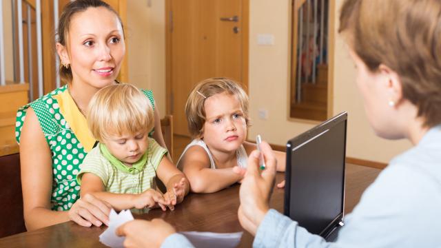 Two children sitting on a person's lap with another person discussing an issue