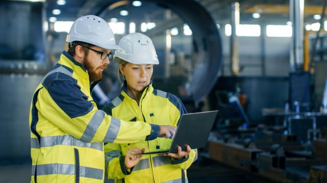 Two workers in hardhats looking at a laptop