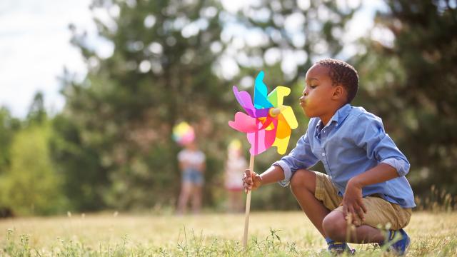 Kid blows into a giant pinwheel at the park