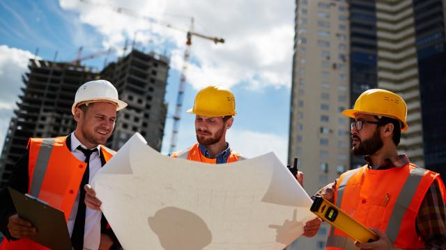 Three workers review the blueprint.