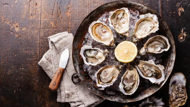 Eight open oysters arranged in a circle on copper plate with sliced lemon in the middle.