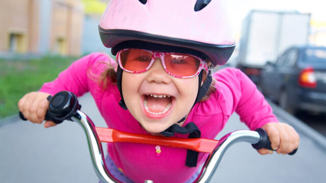 A portrait of a young child wearing a helmet and a pair of sunglasses on a bicycle.