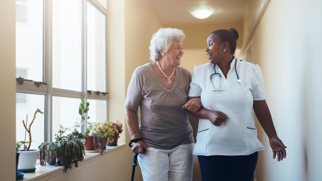 A caregiver assisting an older adult to walk down a hallway