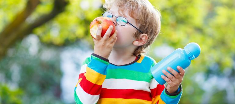 Young child eating an apple and holding water container outdoors.