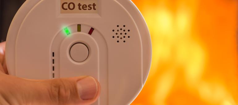 Close up of hands holding a carbon monoxide alarm with a blurred fire background