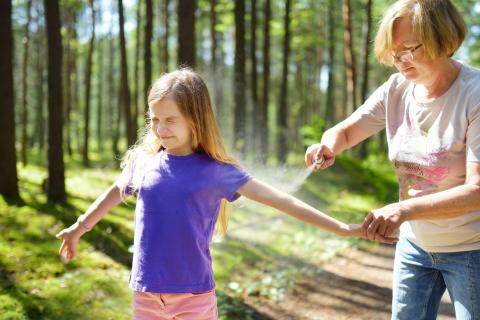 Adult applying insect repellent to a child at a park