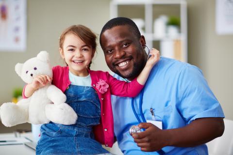 Child hugging a teddy bear with left arm near healthcare provider's neck