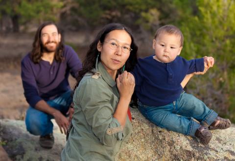 Family of three pose with baby on the rock outside.