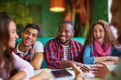 Four teens sitting in a cafe booth talking and laughing