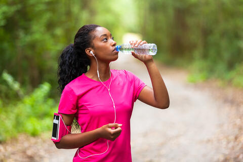 A jogger takes a drink in a park.