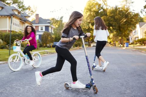 Three children riding bikes and scooters on the street.