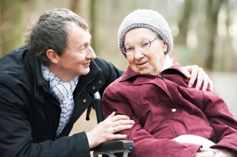 Younger adult comforting an adult in wheelchair outside.