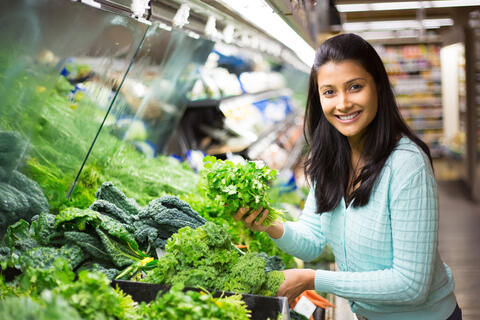 A person chooses cilantro among leafy greens at a grocery store