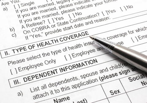 Close up of an insurance form, type of health coverage and dependent information, with a pen resting on the paper