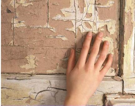 Image of a hand touching a severely flaked wall of lead paint.