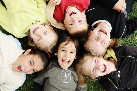 Six children's heads together on grass, all smiling.