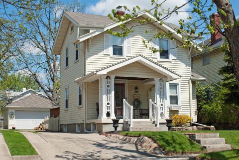 Two story yellow house with white pillars on a lot and a garage in the back