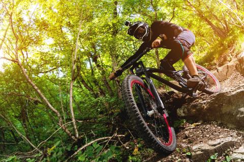 Teen riding mountain bike on rocky ground in forest.